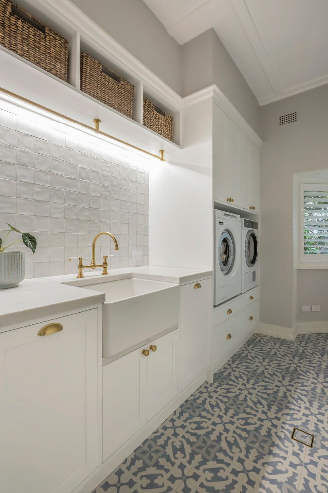 Example of a large single-wall porcelain tile, blue floor and vaulted ceiling laundry closet design in Sydney with a farmhouse sink, shaker cabinets, white cabinets, quartz countertops, white backsplash, ceramic backsplash, gray walls, a side-by-side washer/dryer and white countertops