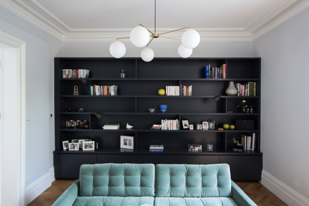 This is an example of an expansive midcentury home office in London with a library, blue walls and medium hardwood floors.