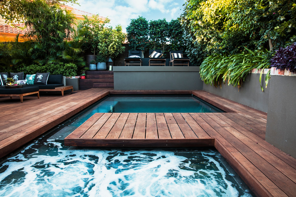 This is an example of a tropical backyard custom-shaped lap pool in Perth with a hot tub and decking.