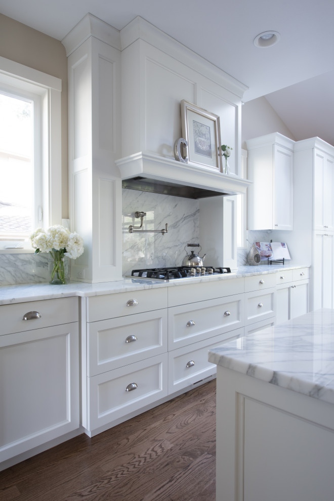 This is an example of a large traditional single-wall open plan kitchen in Seattle with a belfast sink, recessed-panel cabinets, white cabinets, marble worktops, white splashback, marble splashback, stainless steel appliances, dark hardwood flooring, an island, brown floors and white worktops.