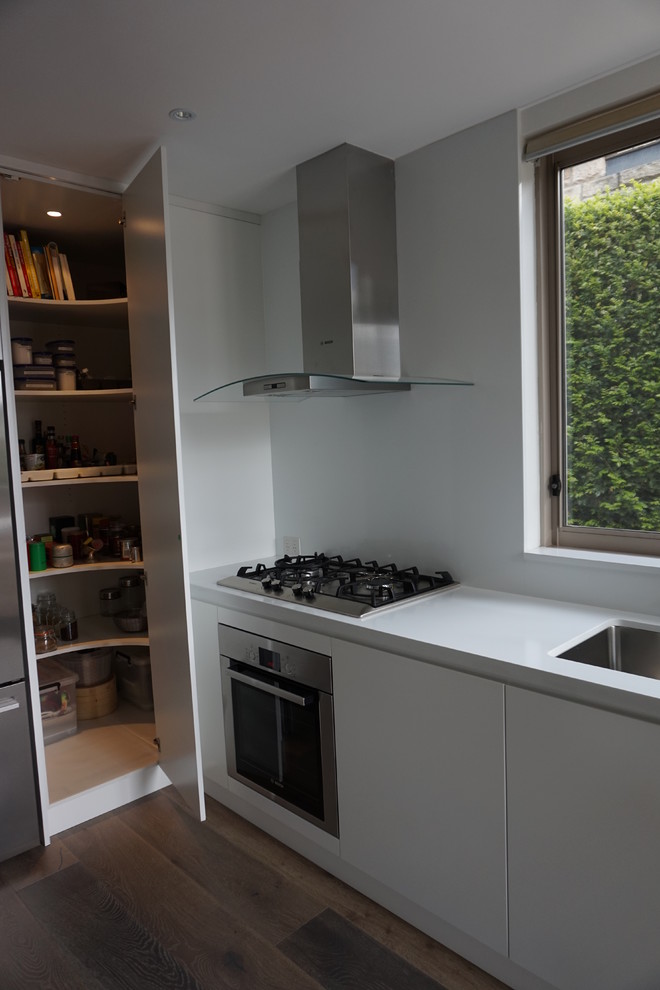 Mid-sized modern l-shaped eat-in kitchen in Sydney with an undermount sink, flat-panel cabinets, white cabinets, quartz benchtops, white splashback, stainless steel appliances, ceramic floors, with island and glass sheet splashback.