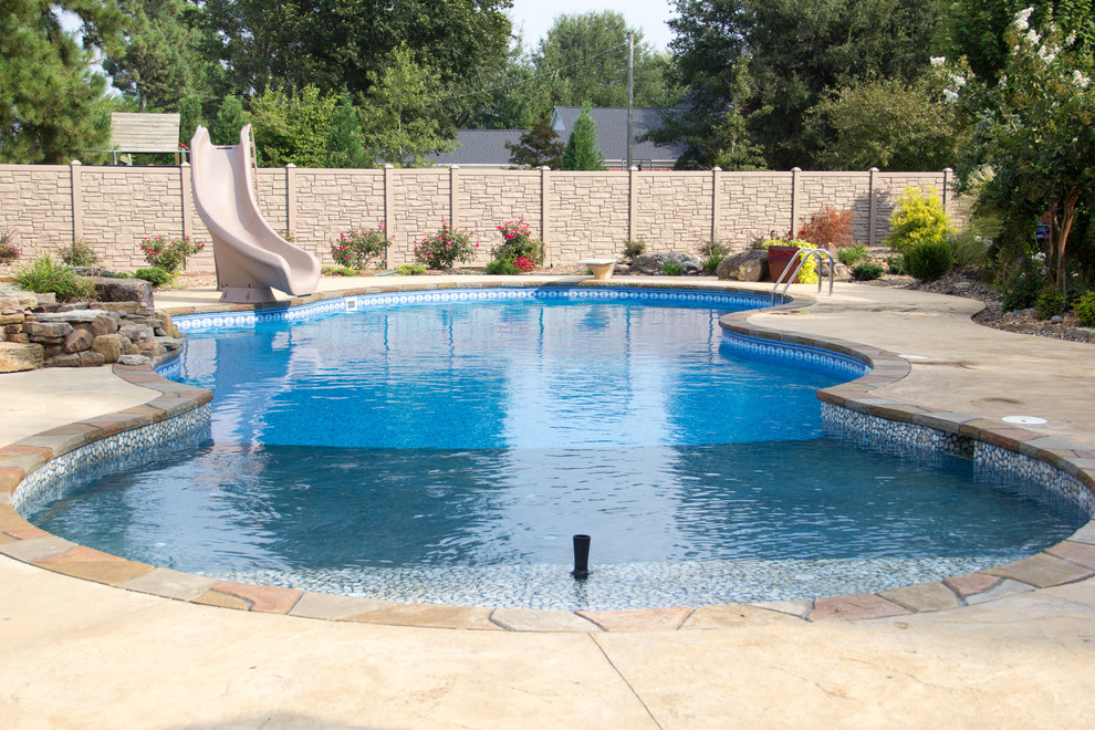 This is an example of a large tropical backyard custom-shaped pool in Chicago with a water feature and stamped concrete.