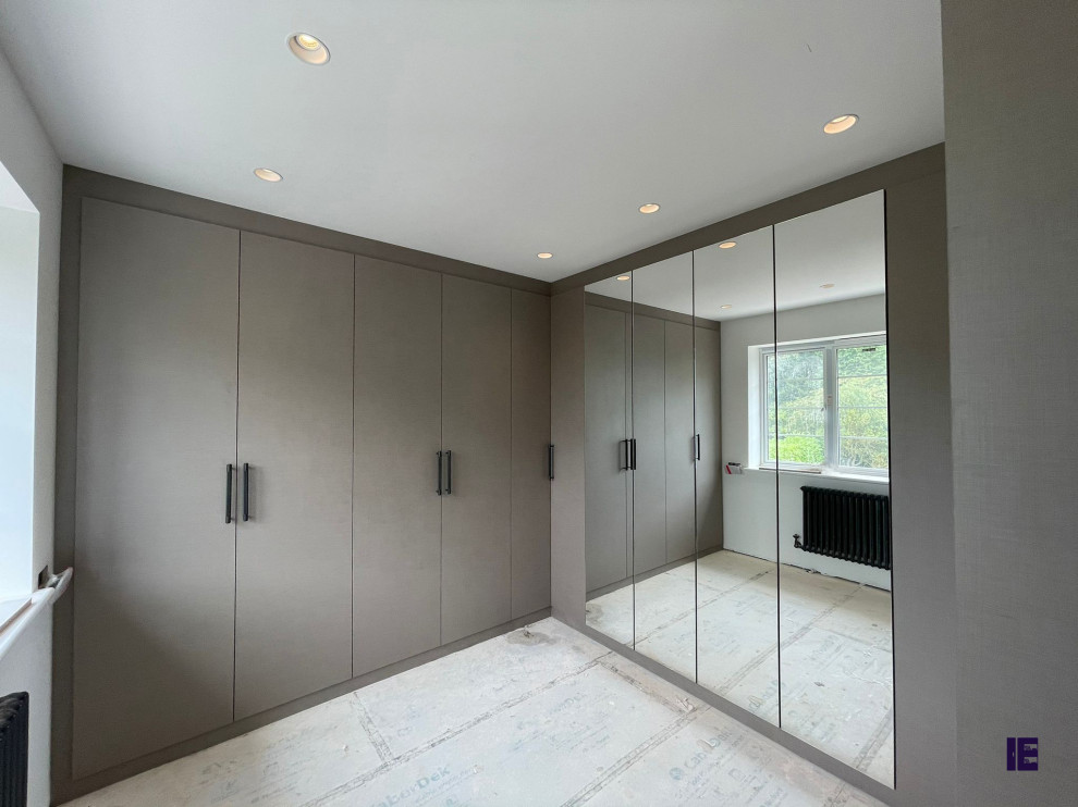 Cette image montre une petite armoire encastrée minimaliste avec un placard avec porte à panneau surélevé, des portes de placard grises et un sol blanc.