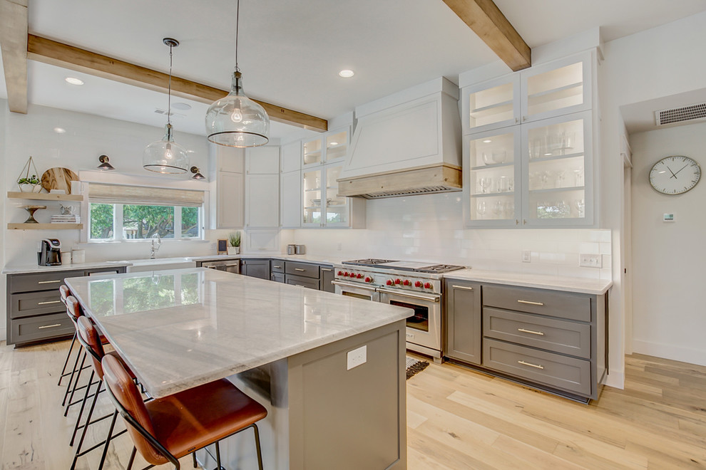 Country l-shaped kitchen in Dallas with a farmhouse sink, shaker cabinets, grey cabinets, white splashback, stainless steel appliances, light hardwood floors, with island, beige floor and white benchtop.