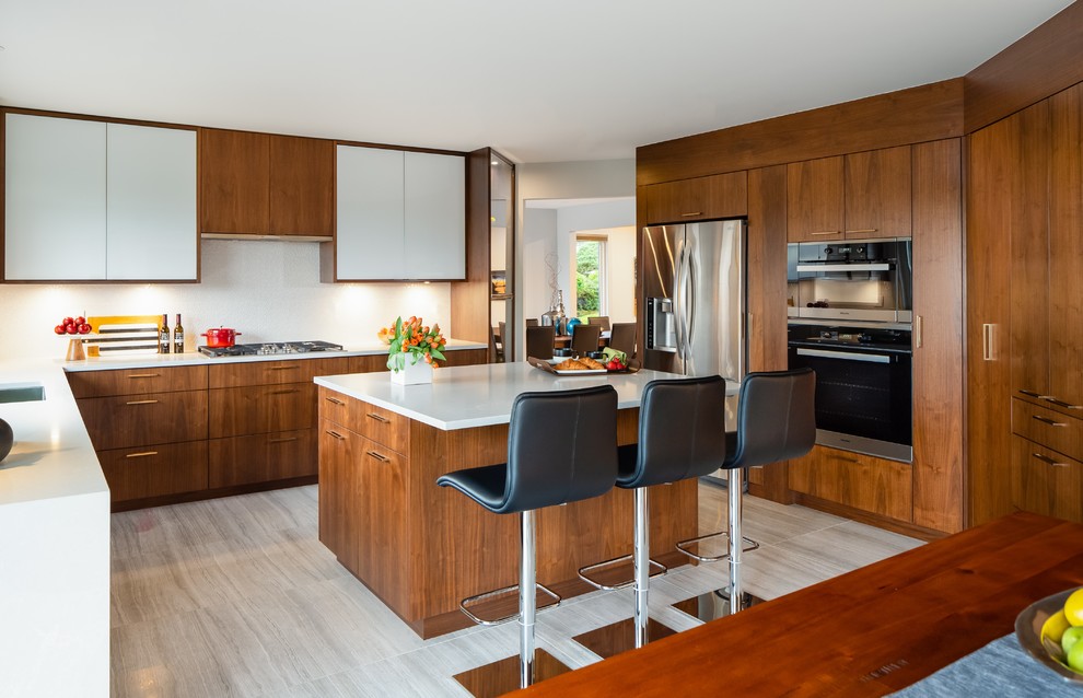 Mid-sized contemporary u-shaped eat-in kitchen in Vancouver with a single-bowl sink, glass-front cabinets, medium wood cabinets, quartz benchtops, white splashback, ceramic splashback, stainless steel appliances, porcelain floors, with island, grey floor and white benchtop.