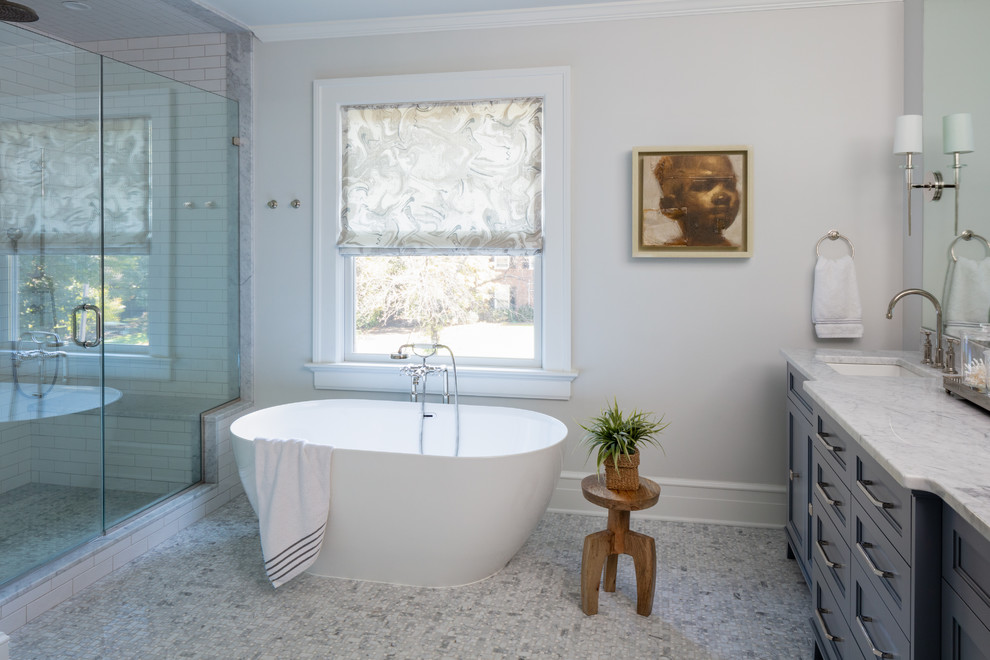 Inspiration for a transitional bathroom in New York with recessed-panel cabinets, blue cabinets, a freestanding tub, an alcove shower, white tile, subway tile, grey walls, marble floors, an undermount sink, grey floor, a hinged shower door and white benchtops.