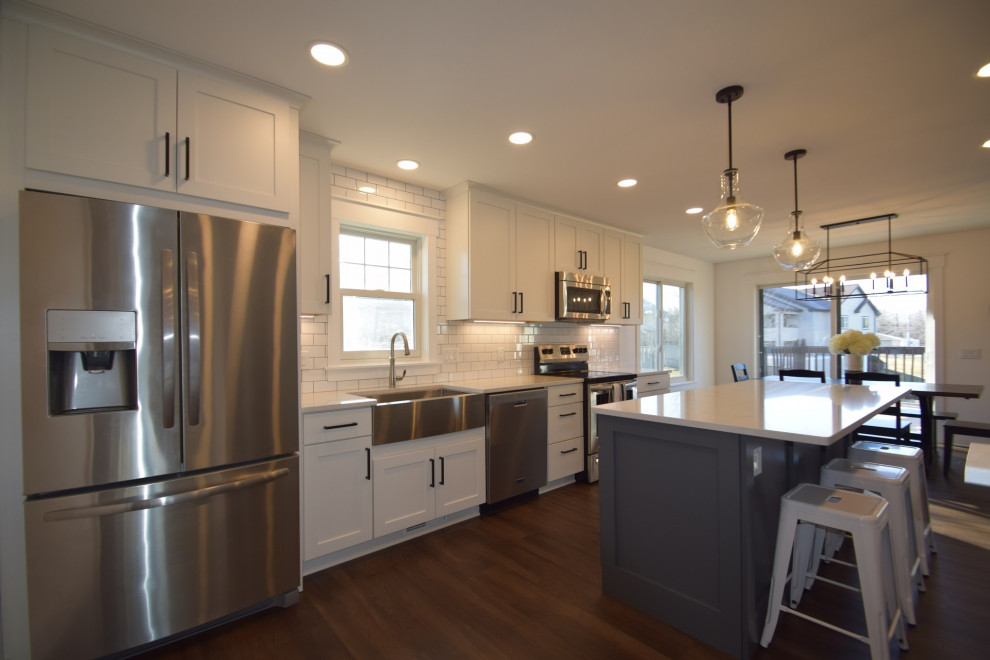 Mid-sized transitional single-wall vinyl floor open concept kitchen photo with a farmhouse sink, shaker cabinets, quartz countertops, white backsplash, subway tile backsplash, stainless steel appliances, an island and white countertops