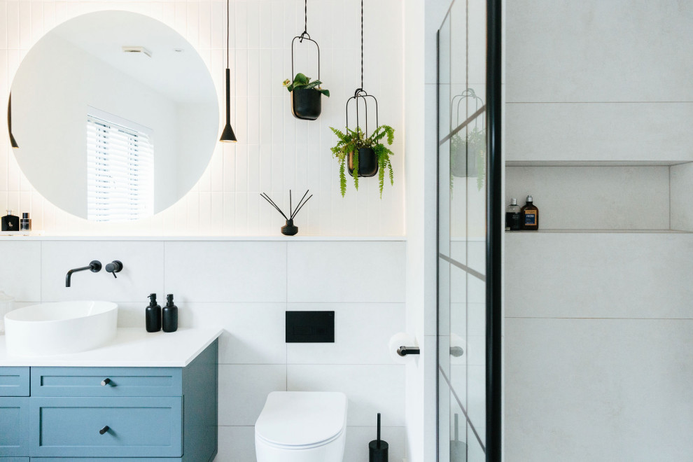 This is an example of a mid-sized transitional kids bathroom in London with shaker cabinets, blue cabinets, a wall-mount toilet, white tile, mosaic tile floors, a drop-in sink, marble benchtops, blue floor, a hinged shower door, white benchtops, a single vanity, a built-in vanity and panelled walls.