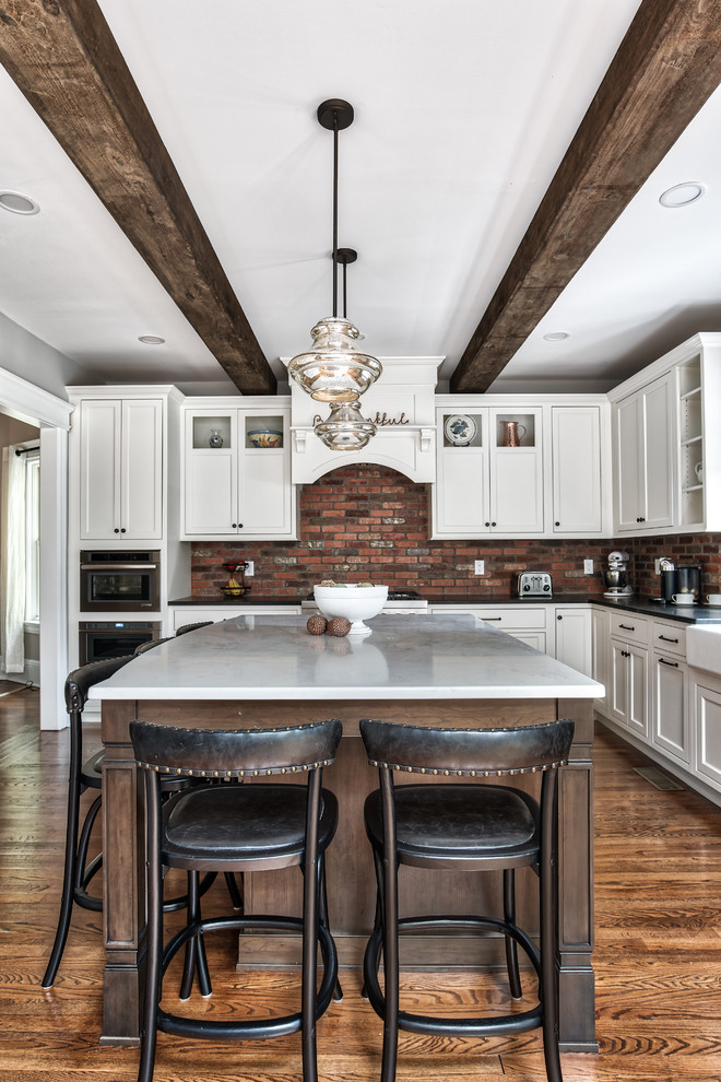 Design ideas for a large country l-shaped eat-in kitchen in New York with a farmhouse sink, beaded inset cabinets, white cabinets, granite benchtops, brick splashback, stainless steel appliances, with island, brown floor, black benchtop and painted wood floors.