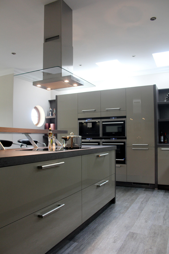 This is an example of a large modern u-shaped open plan kitchen in Glasgow with a double-bowl sink, flat-panel cabinets, stainless steel appliances, with island, black cabinets, glass benchtops, black splashback, glass sheet splashback, dark hardwood floors and black floor.