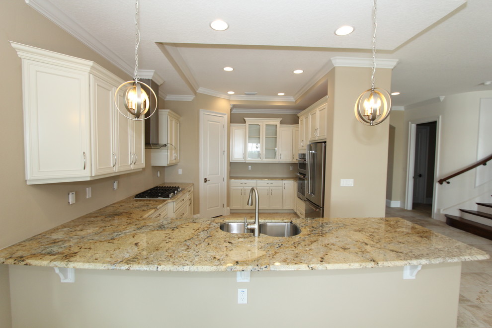 Inspiration for a large mediterranean u-shaped open plan kitchen in Orlando with an undermount sink, raised-panel cabinets, white cabinets, granite benchtops, stainless steel appliances, with island, beige floor and ceramic floors.