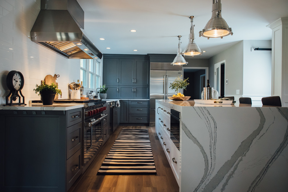 Photo of a large modern l-shaped open plan kitchen in Boston with a farmhouse sink, shaker cabinets, grey cabinets, quartz benchtops, white splashback, ceramic splashback, stainless steel appliances, ceramic floors, with island and brown floor.
