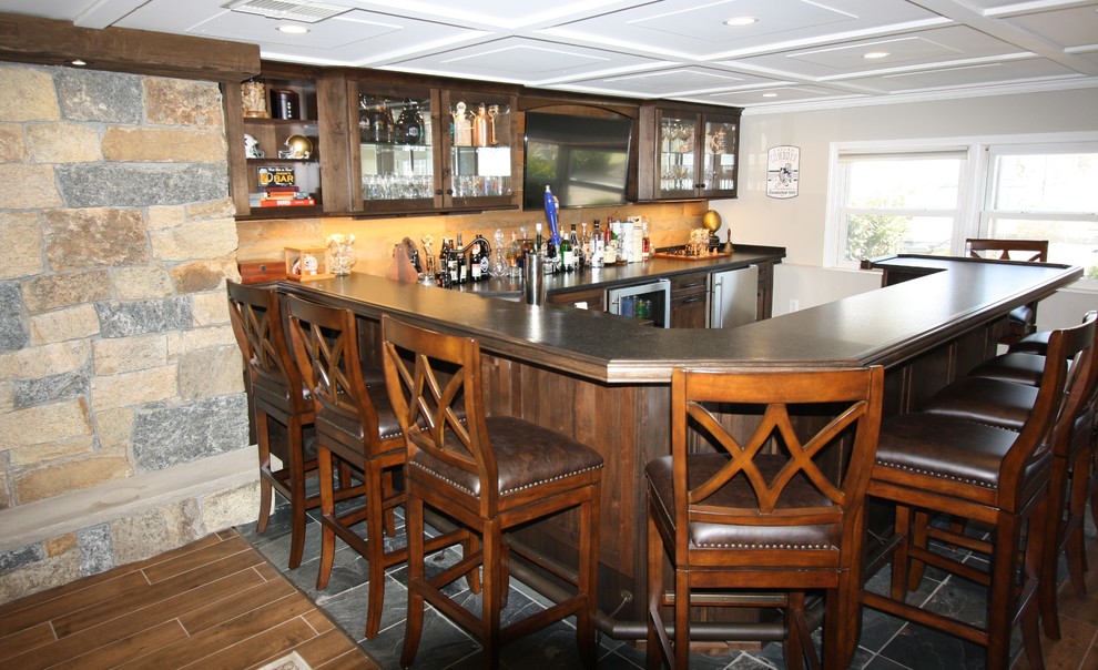 Large traditional u-shaped seated home bar in New York with an undermount sink, glass-front cabinets, dark wood cabinets, granite benchtops, beige splashback, timber splashback, slate floors, multi-coloured floor and black benchtop.