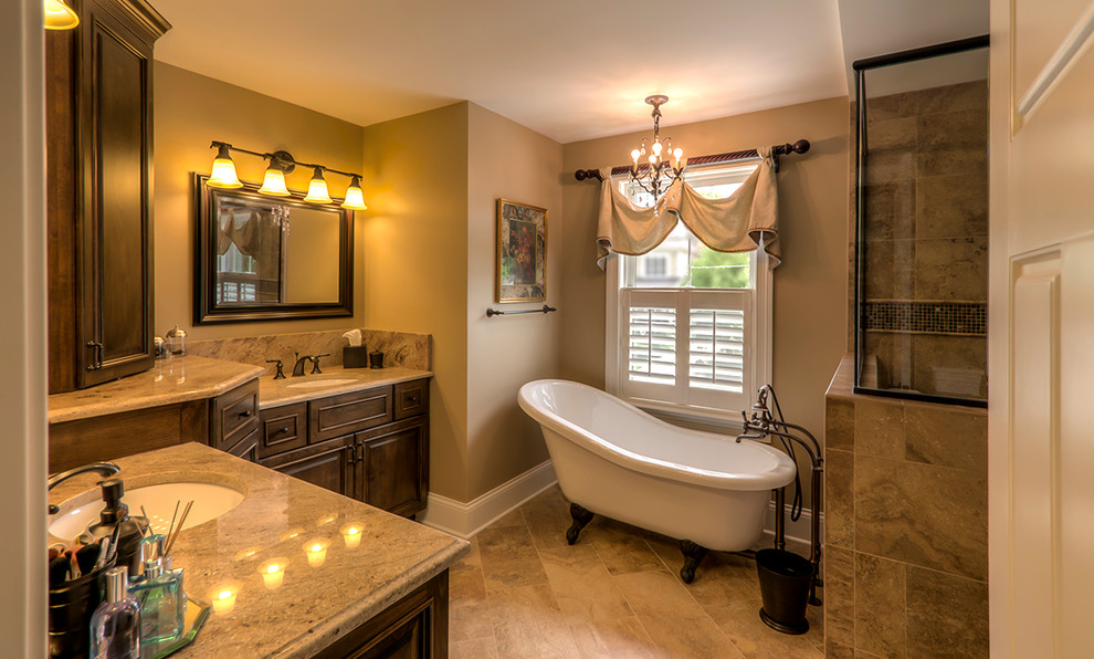 This is an example of a mid-sized traditional master bathroom in Chicago with an undermount sink, raised-panel cabinets, medium wood cabinets, granite benchtops, a claw-foot tub, beige walls, an alcove shower, a one-piece toilet, beige tile, ceramic tile, ceramic floors, brown floor, a hinged shower door, brown benchtops, a double vanity, a freestanding vanity, wallpaper and wallpaper.