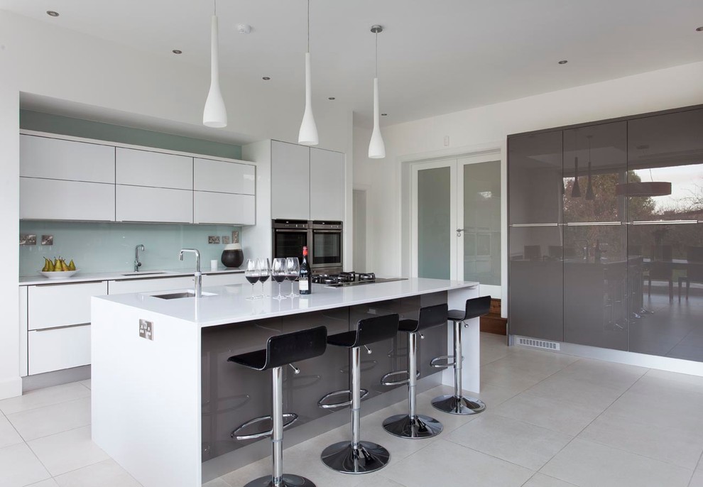 Design ideas for an expansive contemporary open plan kitchen in Dublin with an integrated sink, flat-panel cabinets, white cabinets, quartz benchtops, white splashback, glass sheet splashback, stainless steel appliances, porcelain floors and with island.
