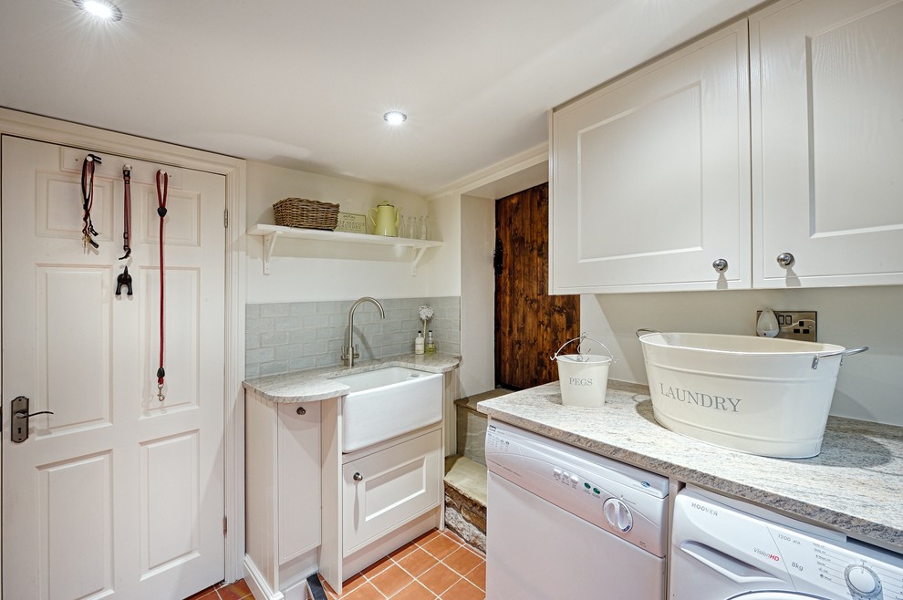 This is an example of a small traditional utility room in Manchester with a farmhouse sink, granite benchtops, white walls and terra-cotta floors.