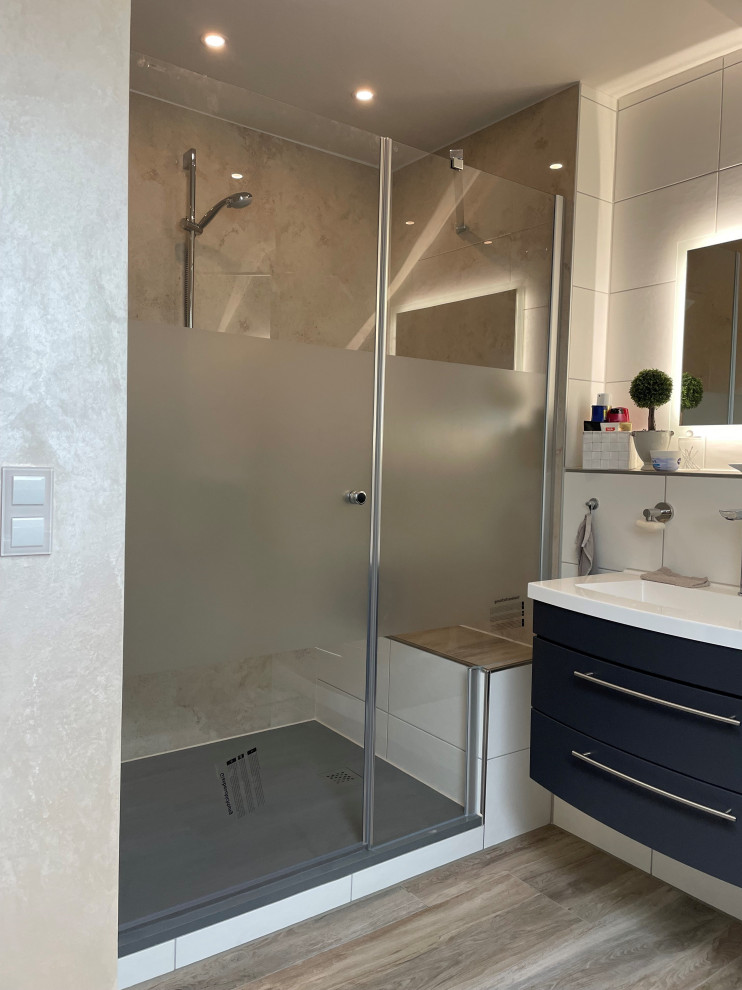 This is an example of a mid-sized contemporary 3/4 bathroom in Other with beaded inset cabinets, blue cabinets, an alcove shower, white tile, porcelain tile, white walls, laminate floors, a drop-in sink, solid surface benchtops, brown floor, a hinged shower door, white benchtops, a single vanity and a freestanding vanity.