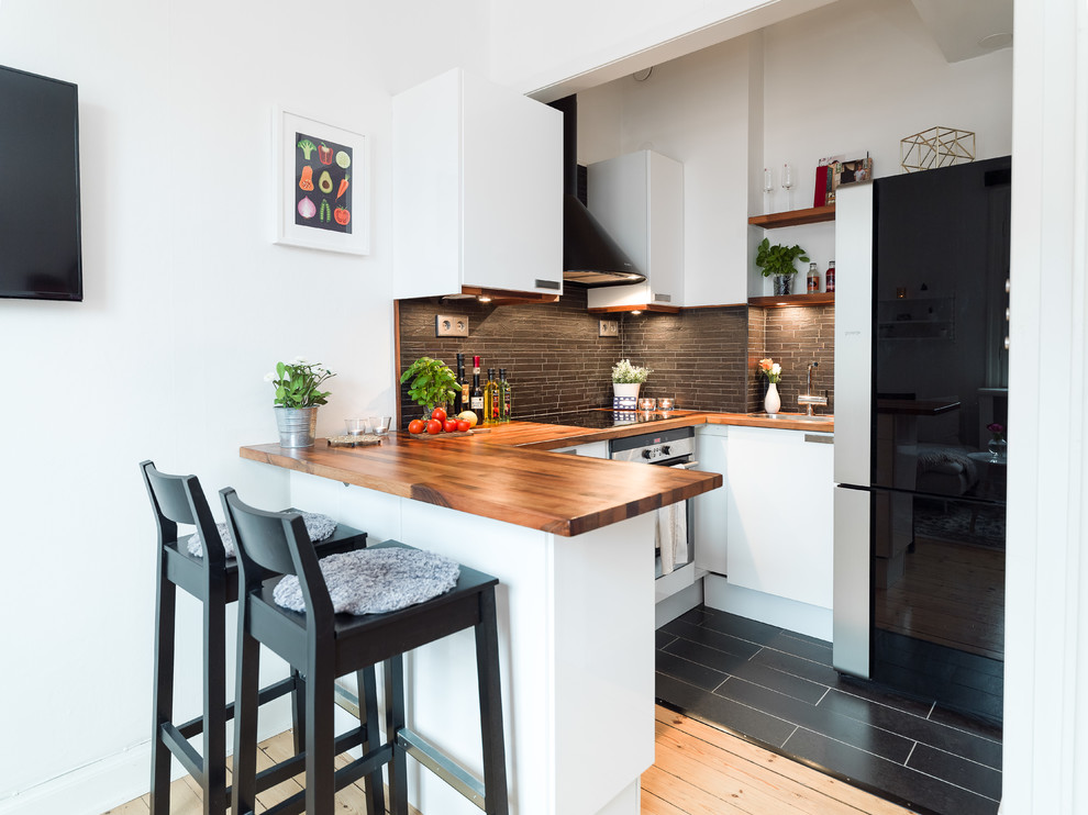 This is an example of a small scandinavian u-shaped kitchen in Stockholm with a single-bowl sink, flat-panel cabinets, white cabinets, wood benchtops, black splashback, matchstick tile splashback and a peninsula.