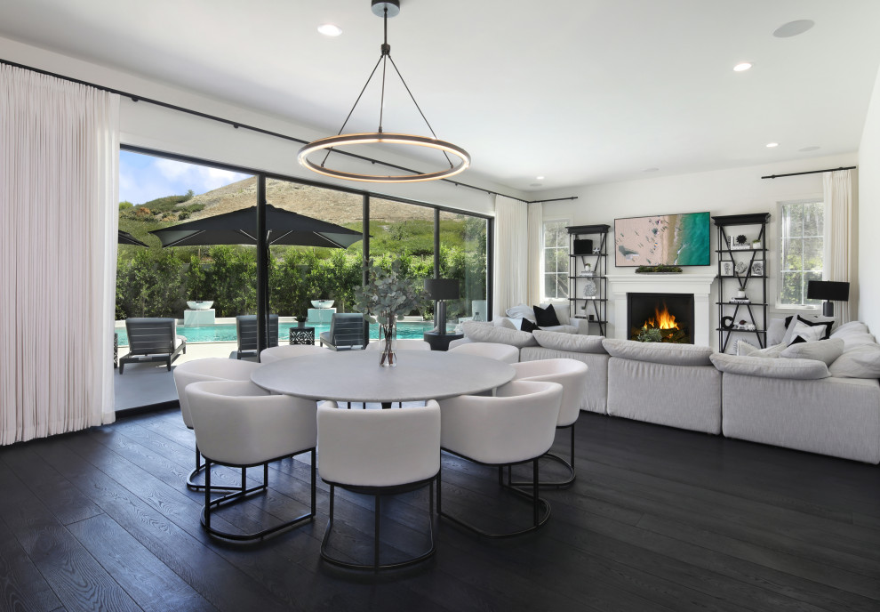 Photo of a large modern kitchen/dining combo in Orange County with white walls, dark hardwood floors, a standard fireplace, a wood fireplace surround and black floor.