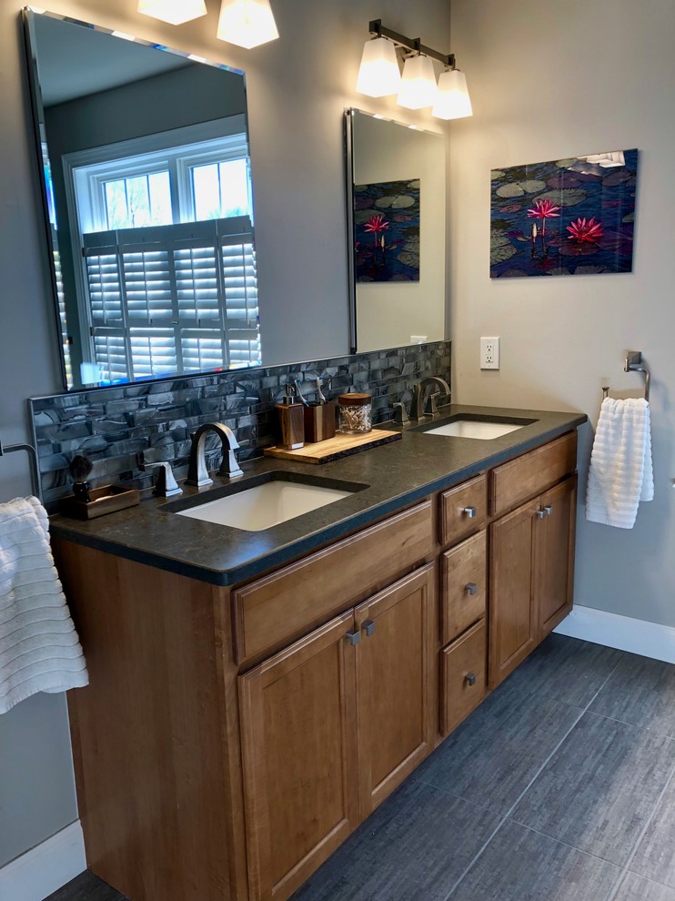 Photo of a mid-sized transitional master bathroom in Philadelphia with shaker cabinets, medium wood cabinets, a curbless shower, a two-piece toilet, gray tile, glass tile, grey walls, porcelain floors, an undermount sink, grey floor, a hinged shower door and grey benchtops.