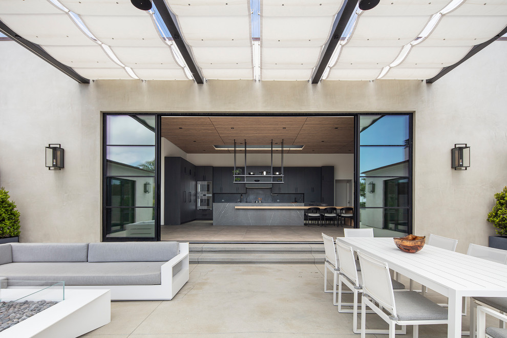 Inspiration for an expansive contemporary courtyard patio in Los Angeles with a fire feature, concrete slabs and an awning.