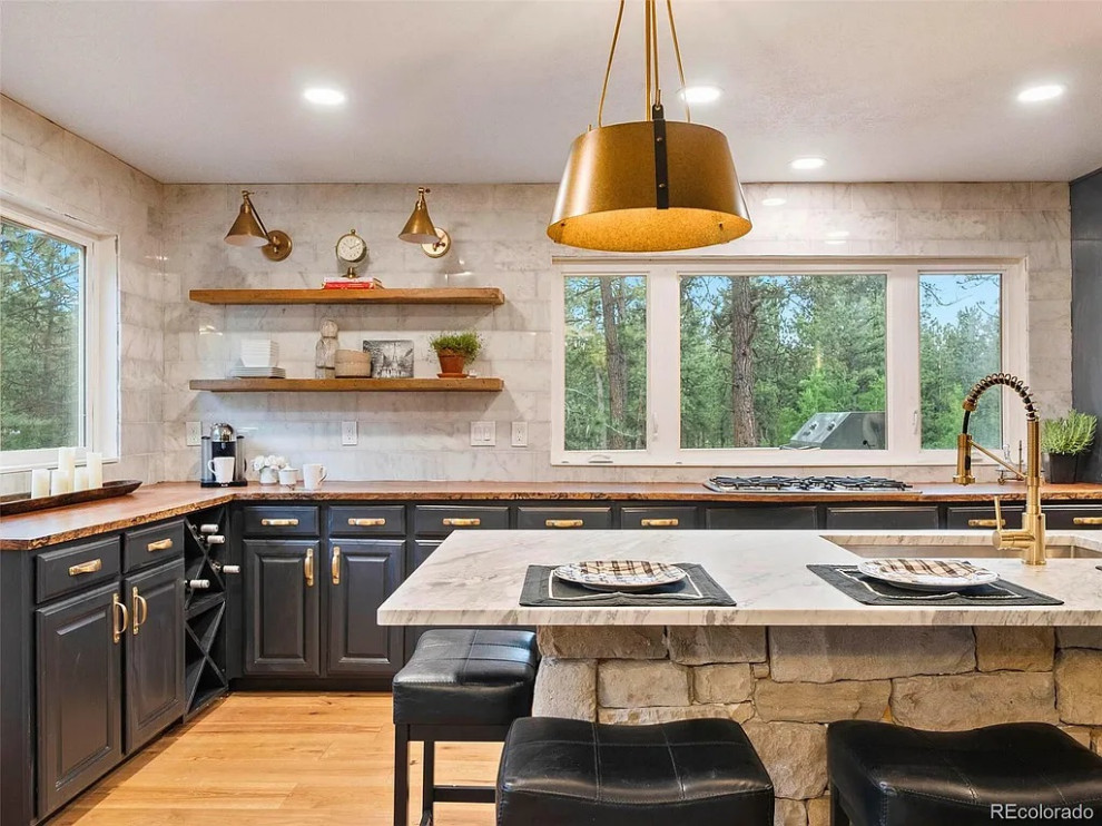 Inspiration for a large transitional u-shaped medium tone wood floor and brown floor open concept kitchen remodel in Denver with an undermount sink, raised-panel cabinets, black cabinets, wood countertops, white backsplash, marble backsplash, stainless steel appliances, an island and brown countertops