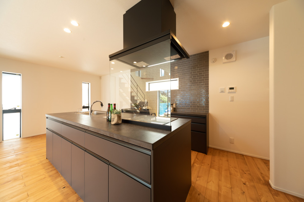 This is an example of an industrial single-wall open plan kitchen in Kobe with grey cabinets, grey splashback, medium hardwood floors, a peninsula, brown floor, grey benchtop and wallpaper.