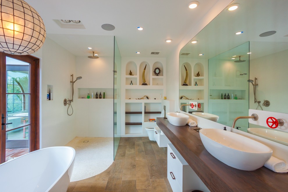 Inspiration for a mid-sized contemporary master bathroom in Los Angeles with white cabinets, a freestanding tub, a curbless shower, a wall-mount toilet, white walls, a vessel sink, wood benchtops, open cabinets, white tile, porcelain tile, medium hardwood floors, brown floor, an open shower and brown benchtops.