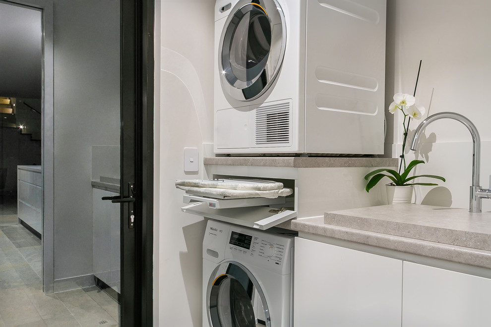 Modern single-wall dedicated laundry room in Perth with an undermount sink, beaded inset cabinets, white cabinets, laminate benchtops, white walls, marble floors, a stacked washer and dryer, grey floor and grey benchtop.