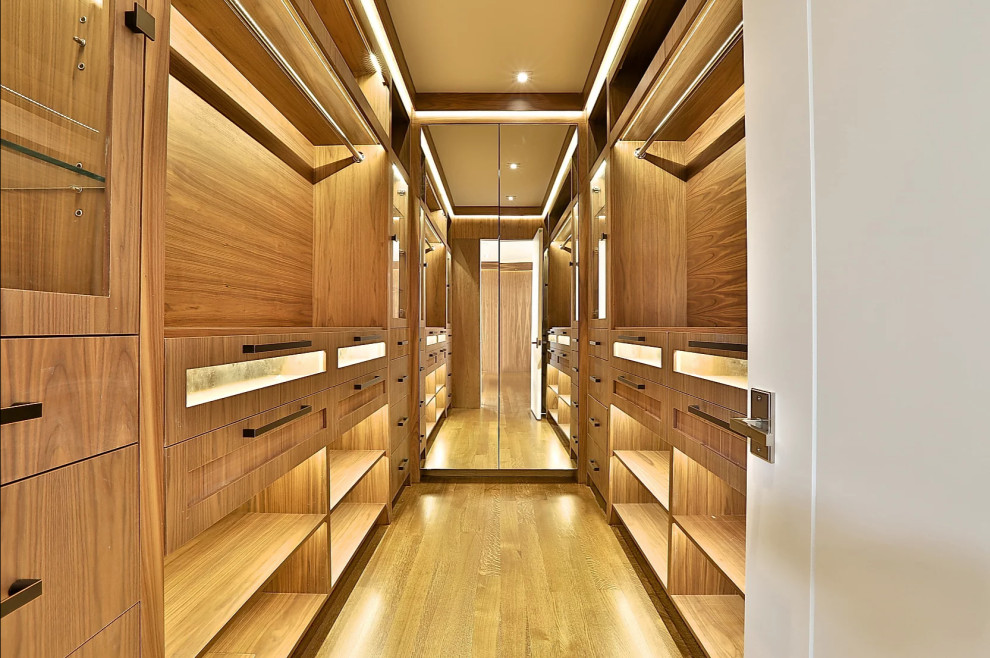 Photo of a large modern men's storage and wardrobe in Toronto with flat-panel cabinets, dark wood cabinets, medium hardwood floors, brown floor and recessed.