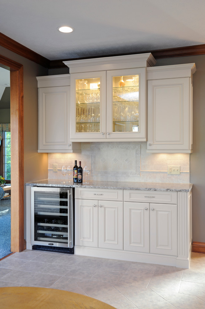 Photo of a mid-sized traditional single-wall wet bar in Other with no sink, raised-panel cabinets, white cabinets, granite benchtops, beige splashback, stone tile splashback and ceramic floors.