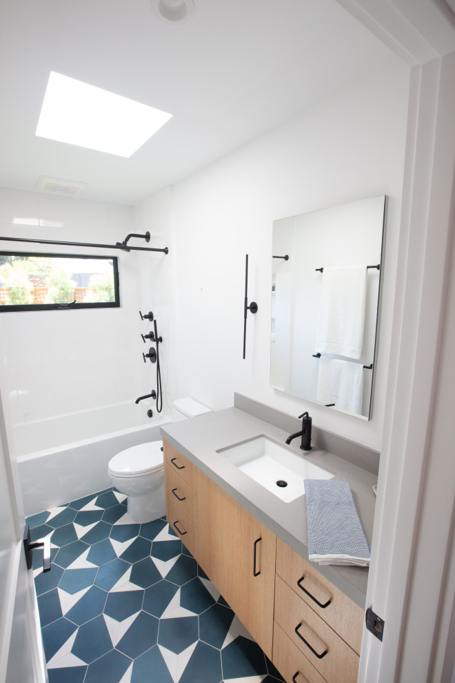 Photo of a medium sized family bathroom in San Francisco with flat-panel cabinets, light wood cabinets, an alcove bath, a shower/bath combination, a two-piece toilet, white tiles, metro tiles, white walls, porcelain flooring, a submerged sink, engineered stone worktops, multi-coloured floors, a shower curtain, grey worktops, a single sink and a floating vanity unit.