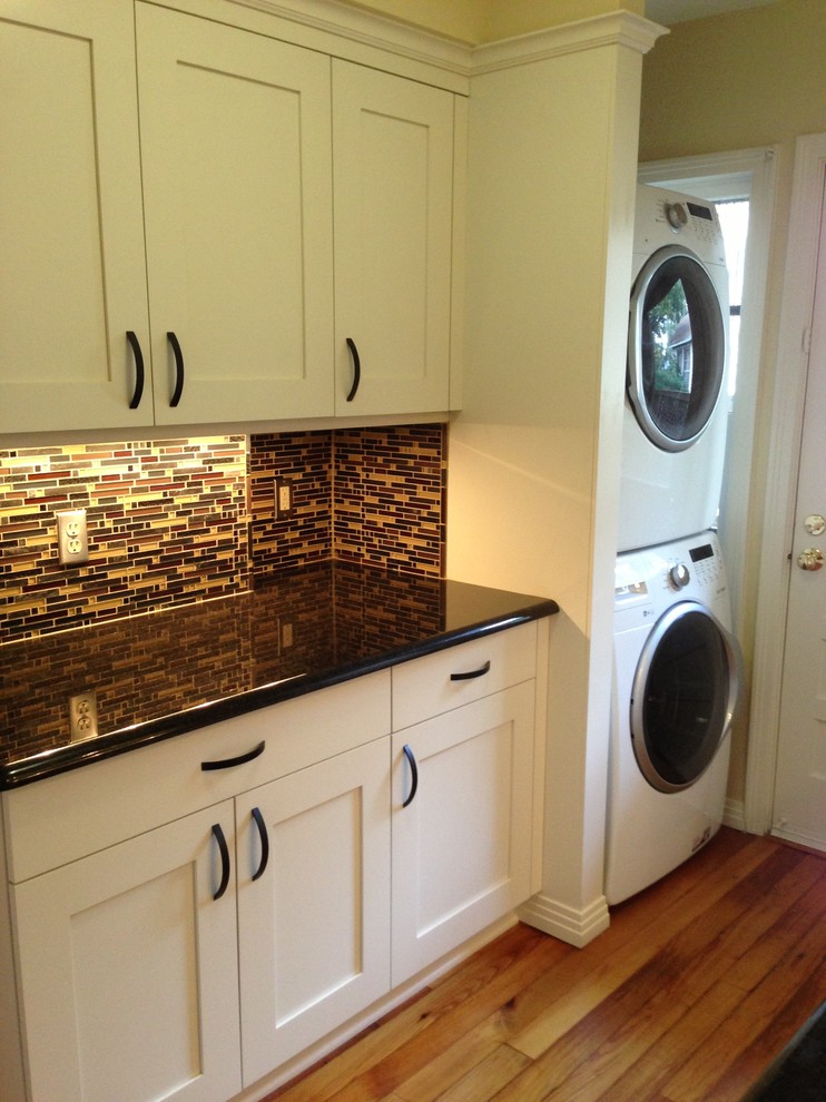 Inspiration for a small eclectic l-shaped laundry room in Austin with shaker cabinets, white cabinets, granite benchtops, medium hardwood floors, a stacked washer and dryer and beige walls.
