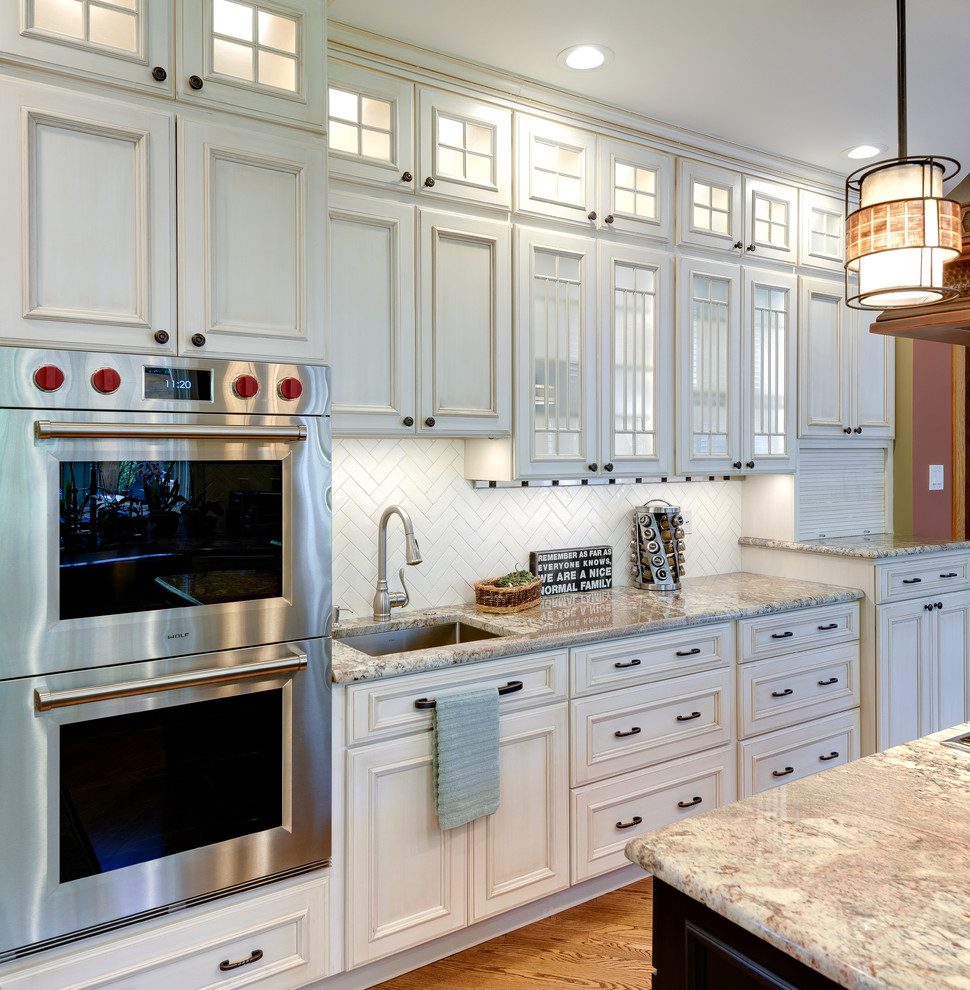 Inspiration for a large traditional l-shaped eat-in kitchen in Philadelphia with an undermount sink, beaded inset cabinets, distressed cabinets, white splashback, subway tile splashback, stainless steel appliances, light hardwood floors, with island, brown floor, multi-coloured benchtop and granite benchtops.