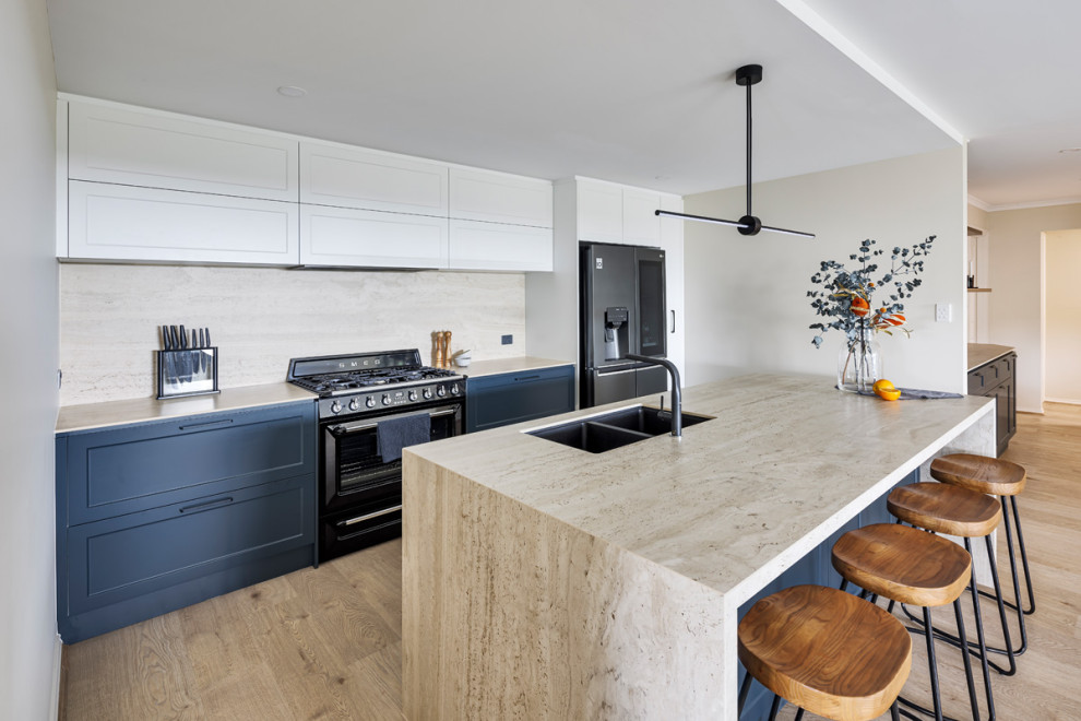 Contemporary kitchen in Other with a double-bowl sink, shaker cabinets, blue cabinets, beige splashback, travertine splashback, black appliances and beige worktops.