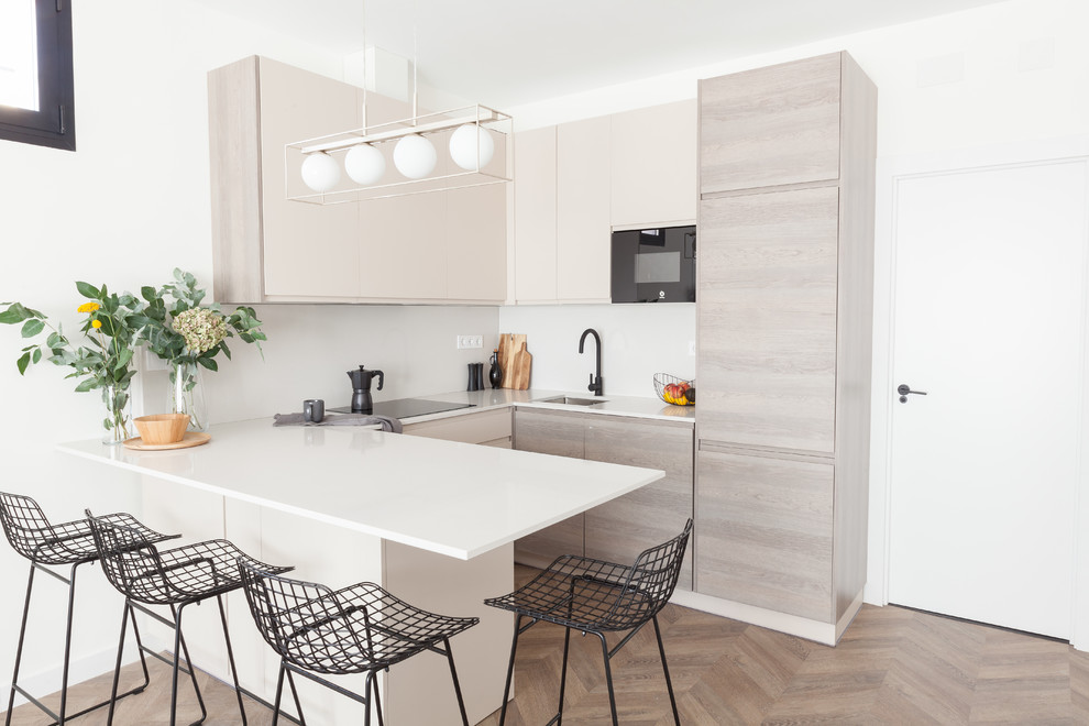This is an example of a mid-sized scandinavian u-shaped open plan kitchen in Madrid with an undermount sink, flat-panel cabinets, beige cabinets, quartz benchtops, beige splashback, limestone splashback, black appliances, laminate floors, a peninsula, brown floor and beige benchtop.