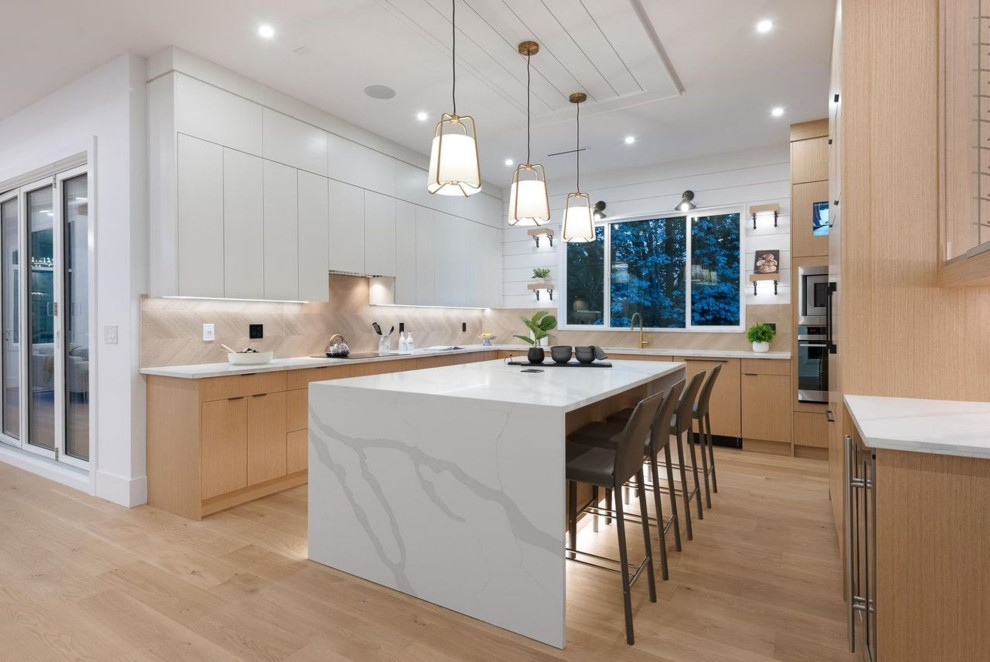 Large contemporary u-shaped kitchen in Vancouver with a double-bowl sink, flat-panel cabinets, beige cabinets, terrazzo benchtops, beige splashback, porcelain splashback, stainless steel appliances, limestone floors, with island, beige floor, white benchtop and vaulted.