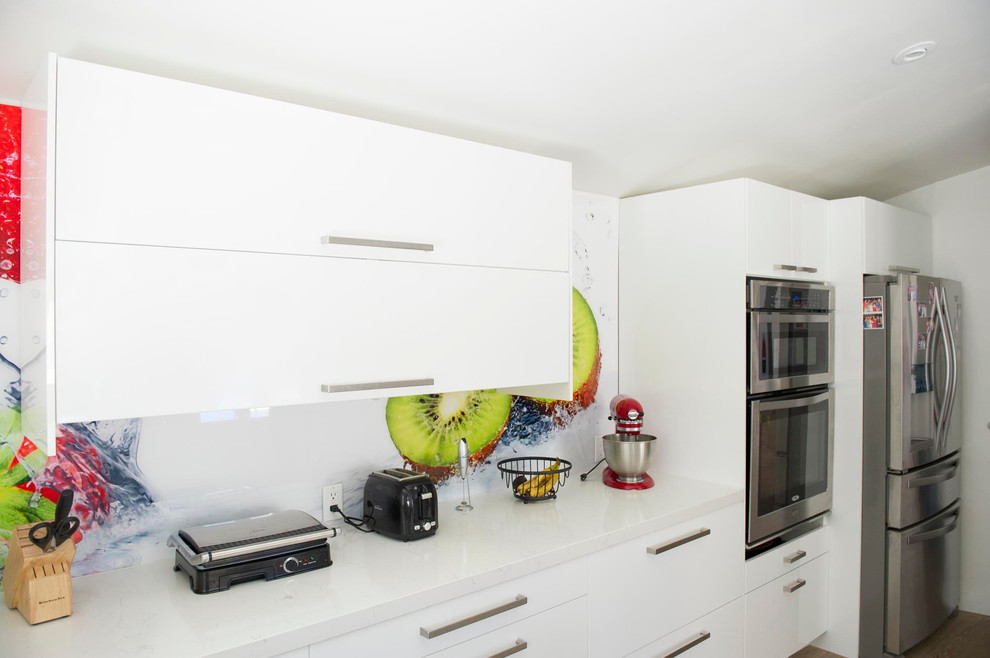 This is an example of a mid-sized modern u-shaped open plan kitchen in Los Angeles with an undermount sink, flat-panel cabinets, white cabinets, quartz benchtops, multi-coloured splashback, stainless steel appliances, light hardwood floors and a peninsula.