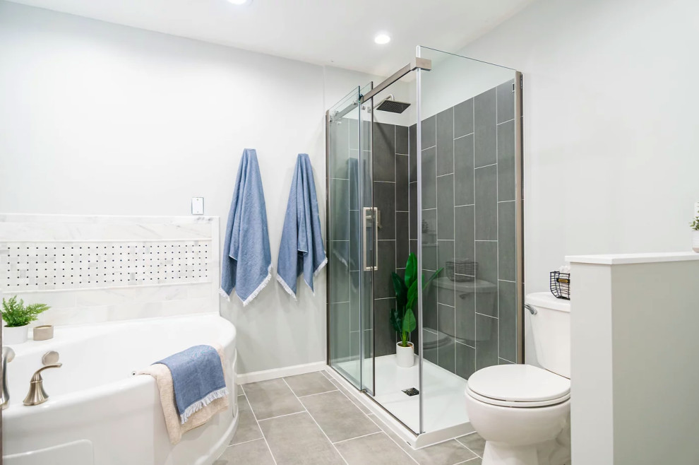 Inspiration for a medium sized traditional ensuite bathroom in Minneapolis with flat-panel cabinets, medium wood cabinets, a corner bath, a corner shower, a one-piece toilet, grey tiles, grey walls, ceramic flooring, a submerged sink, engineered stone worktops, grey floors, a sliding door, white worktops, double sinks and a freestanding vanity unit.