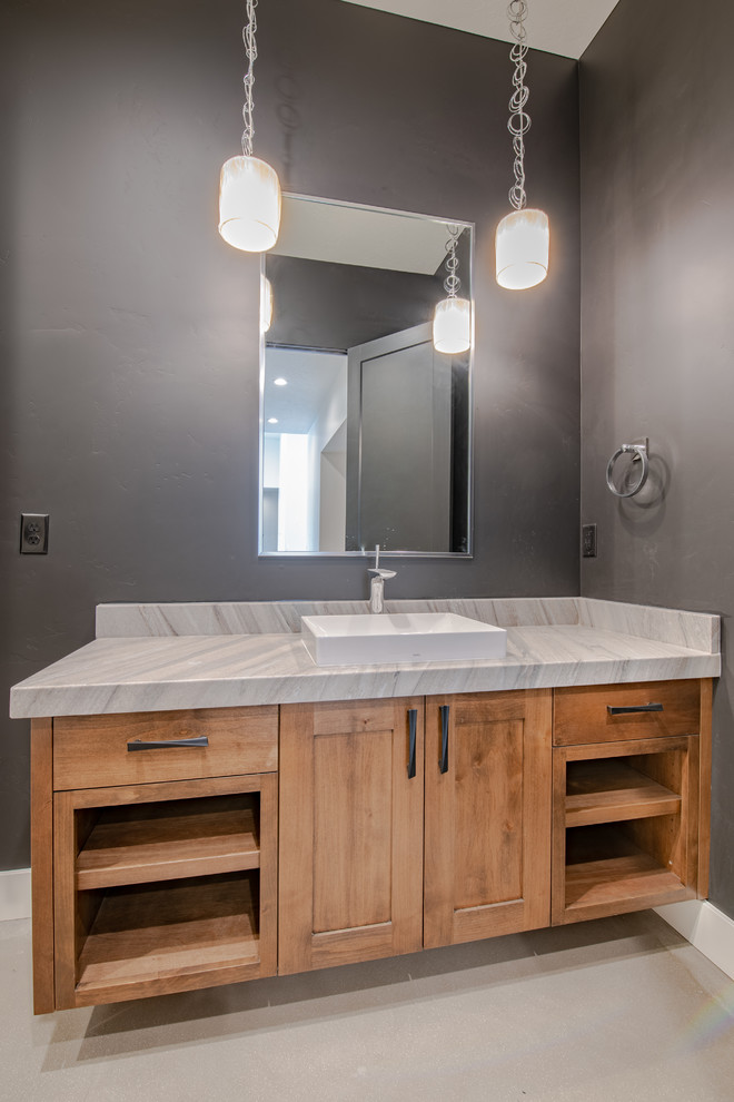 Large country powder room in Salt Lake City with flat-panel cabinets, medium wood cabinets, a two-piece toilet, black tile, stone slab, black walls, concrete floors, a vessel sink, quartzite benchtops, grey floor and beige benchtops.