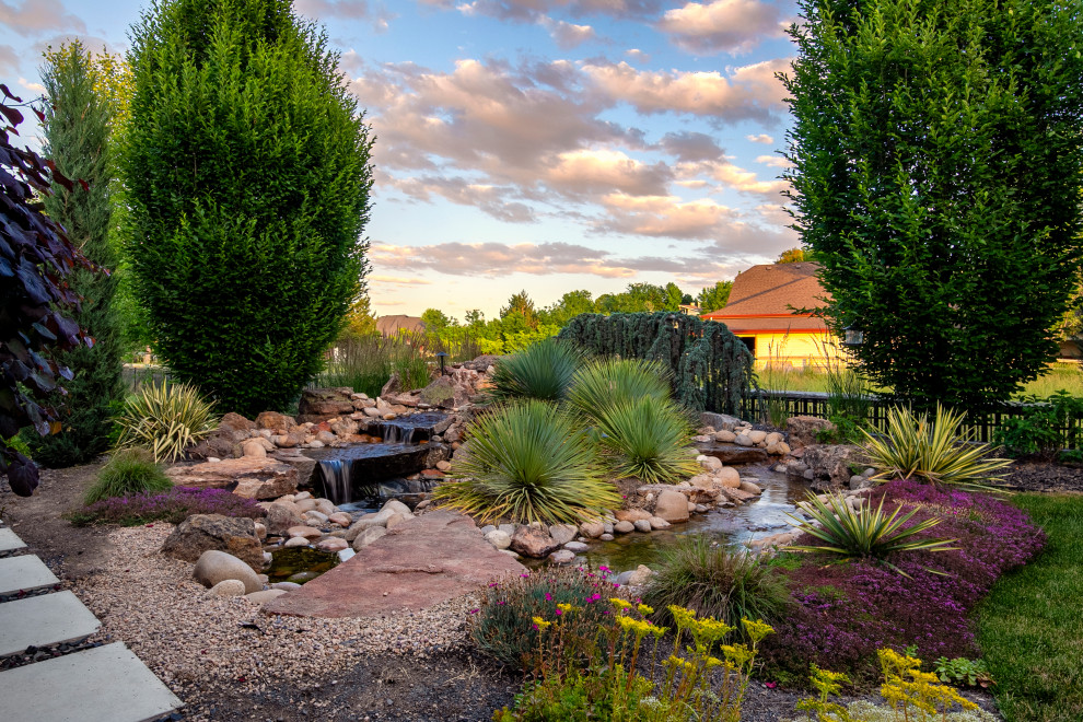 Photo of a large modern side garden for spring in Boise with a pond, concrete paving and a metal fence.