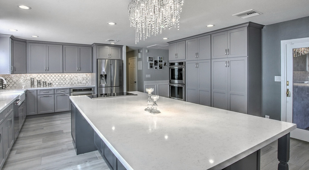 This is an example of an expansive transitional l-shaped eat-in kitchen in Phoenix with a farmhouse sink, shaker cabinets, grey cabinets, quartz benchtops, white splashback, mirror splashback, stainless steel appliances, porcelain floors and with island.