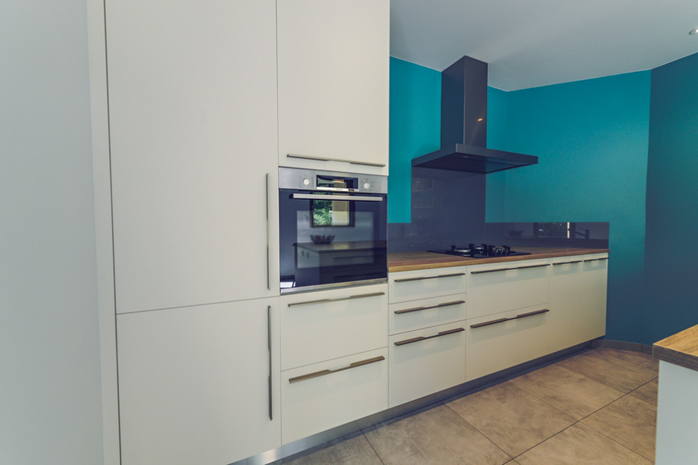 This is an example of a mid-sized contemporary galley separate kitchen in Rennes with a single-bowl sink, beaded inset cabinets, white cabinets, laminate benchtops, grey splashback, glass sheet splashback, stainless steel appliances, ceramic floors, a peninsula and grey floor.