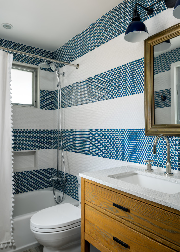 Photo of a small beach style 3/4 bathroom in Hawaii with flat-panel cabinets, medium wood cabinets, an alcove tub, a shower/bathtub combo, a one-piece toilet, blue tile, ceramic tile, blue walls, porcelain floors, an undermount sink, engineered quartz benchtops, grey floor, a shower curtain, white benchtops, a single vanity and a freestanding vanity.
