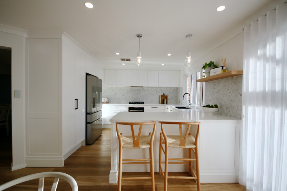 Photo of a mid-sized modern u-shaped eat-in kitchen in Sydney with an undermount sink, shaker cabinets, white cabinets, quartz benchtops, grey splashback, marble splashback, black appliances, medium hardwood floors, with island, brown floor and white benchtop.