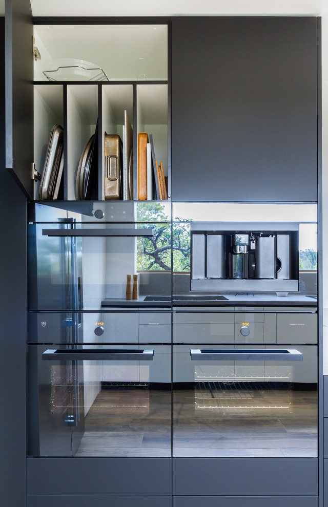 Inspiration for an expansive modern u-shaped eat-in kitchen in Melbourne with a double-bowl sink, flat-panel cabinets, black cabinets, quartz benchtops, white splashback, window splashback, stainless steel appliances, porcelain floors, with island, brown floor and white benchtop.