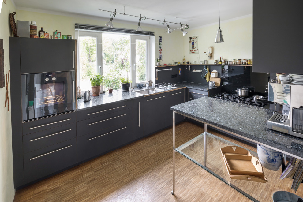 Geschlossene, Mittelgroße Industrial Küche in L-Form mit Doppelwaschbecken, grauen Schränken, Granit-Arbeitsplatte und schwarzen Elektrogeräten in Stuttgart