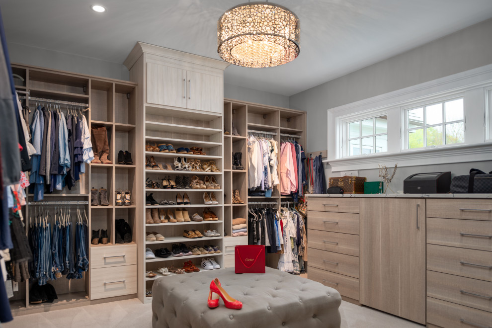 This is an example of a transitional women's walk-in wardrobe in Providence with flat-panel cabinets, light wood cabinets and beige floor.