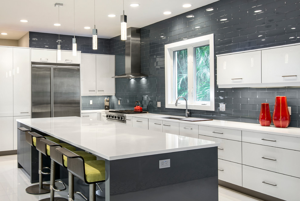 Photo of a contemporary l-shaped eat-in kitchen in Miami with flat-panel cabinets, white cabinets, grey splashback, stainless steel appliances, glass tile splashback, an undermount sink, solid surface benchtops, porcelain floors and with island.