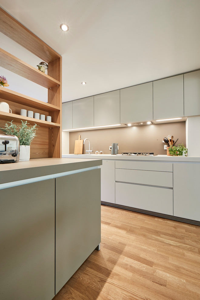 Inspiration for a mid-sized contemporary single-wall open plan kitchen in Hamburg with a drop-in sink, flat-panel cabinets, beige splashback, light hardwood floors, beige floor, beige cabinets, laminate benchtops, stainless steel appliances, a peninsula and beige benchtop.